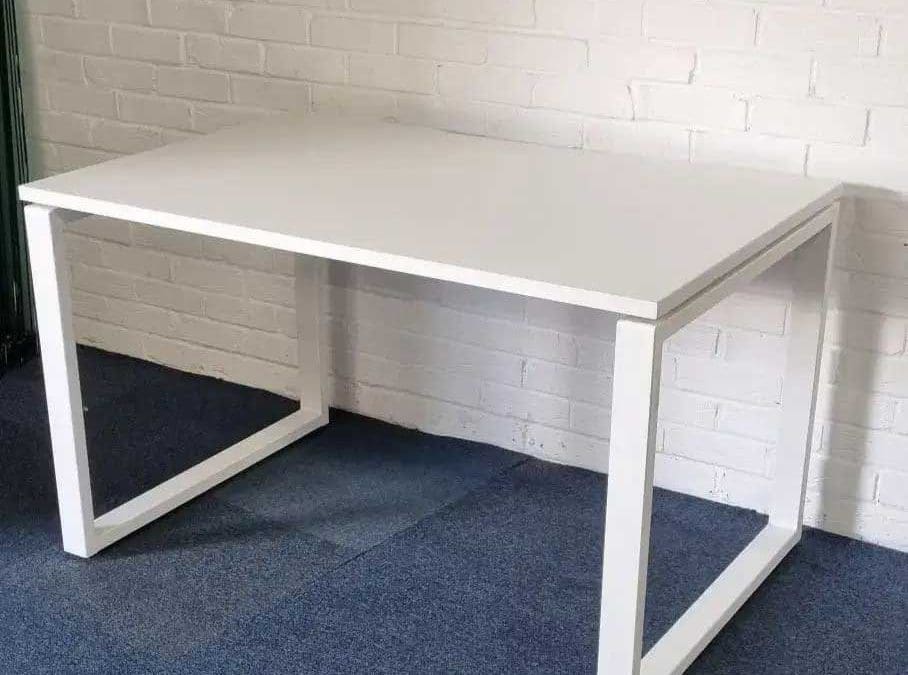 Minimalist white office desk with metal frame against a white brick wall.
